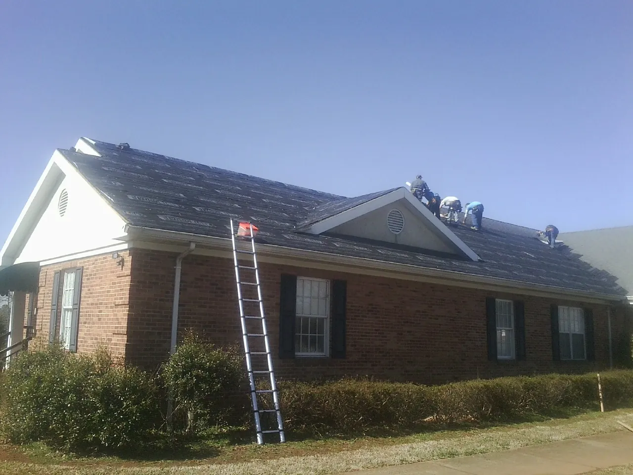 Crew tearing shingles off a brick ranch roof with a ladder set — Emergency Roof Repair work by our crew in Sharon Hill