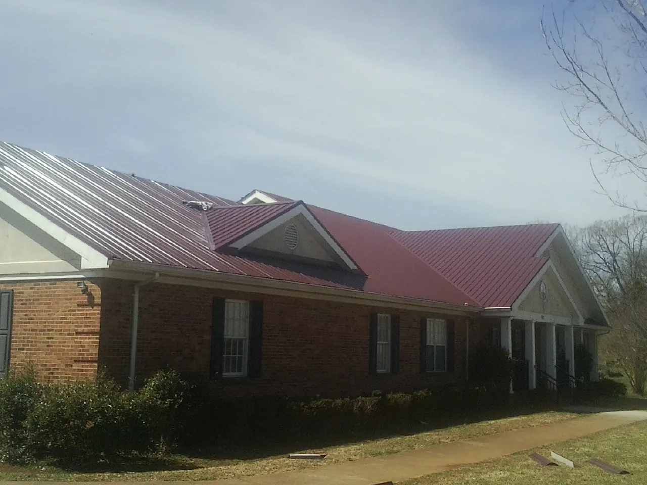 Red metal roof with gabled entries on a long brick building, from a Hail Damage Roof Repair job in Sharon Hill