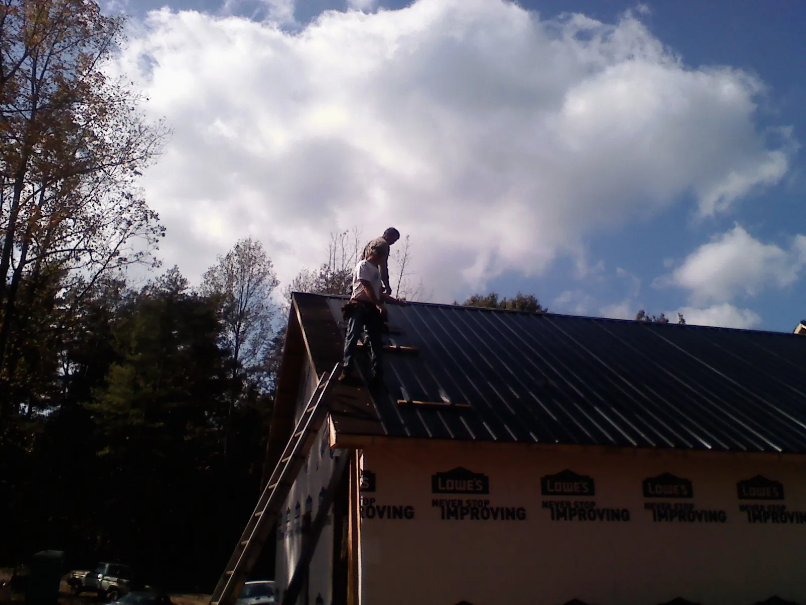 Roofer fastening dark metal panels high against a cloudy sky, from a Roof Inspection job in Sharon Hill