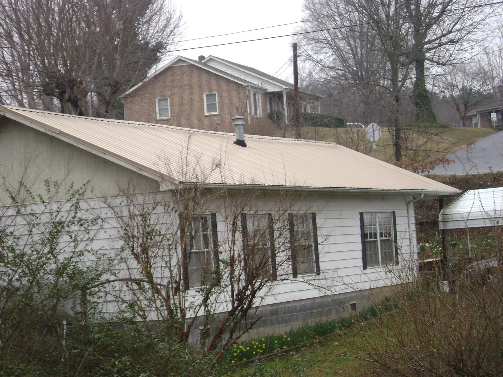 Tan metal roof on a white sided house set into a hillside — Commercial Roofing by Roofing Brothers in Sharon Hill