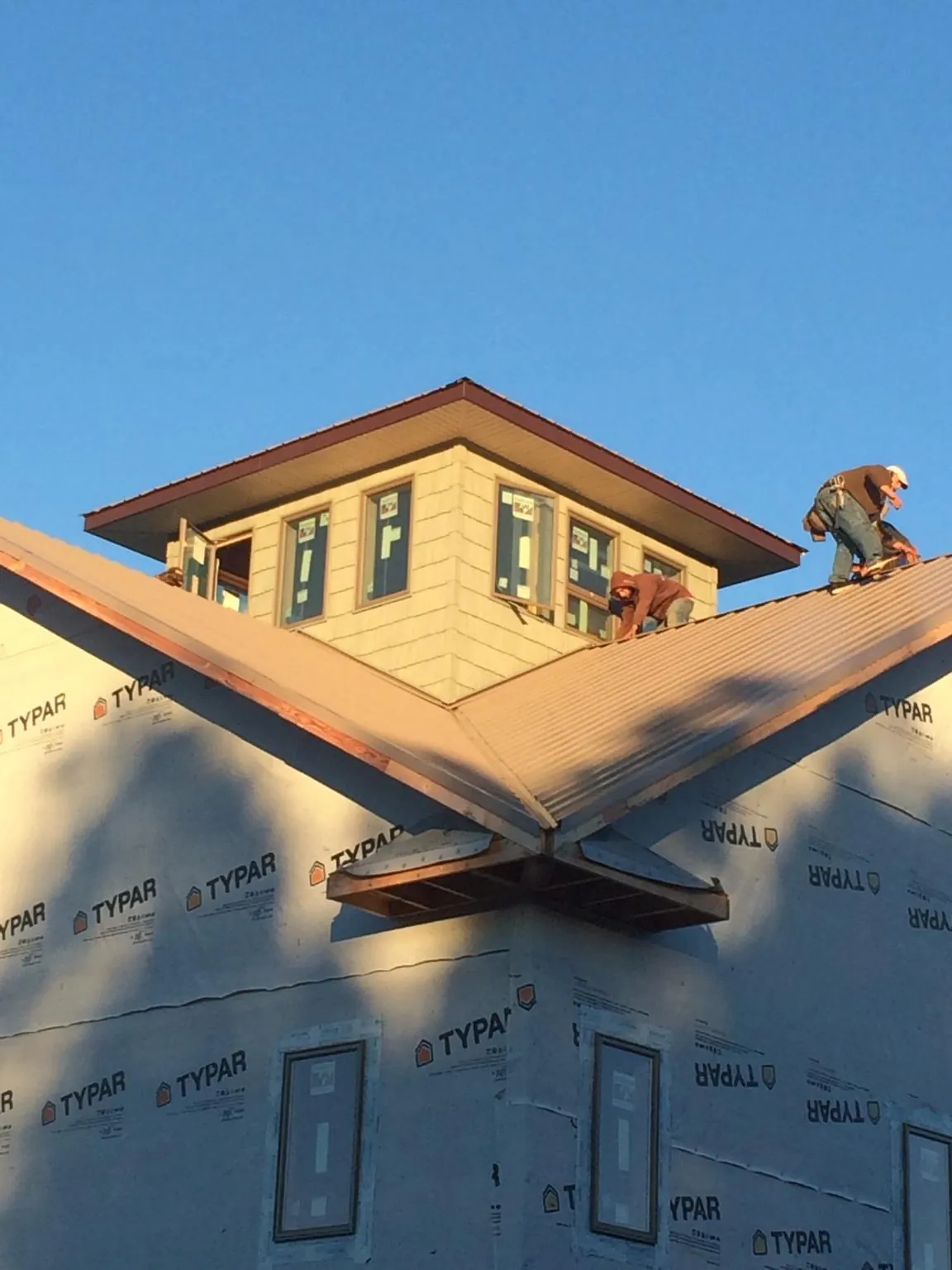 Roofers working around a rooftop cupola on a new metal roof at sunset — Roof Waterproofing in Sharon Hill by Roofing Brothers